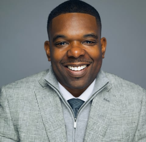 Portrait of a smiling man in a light gray plaid blazer and blue tie against a gray background